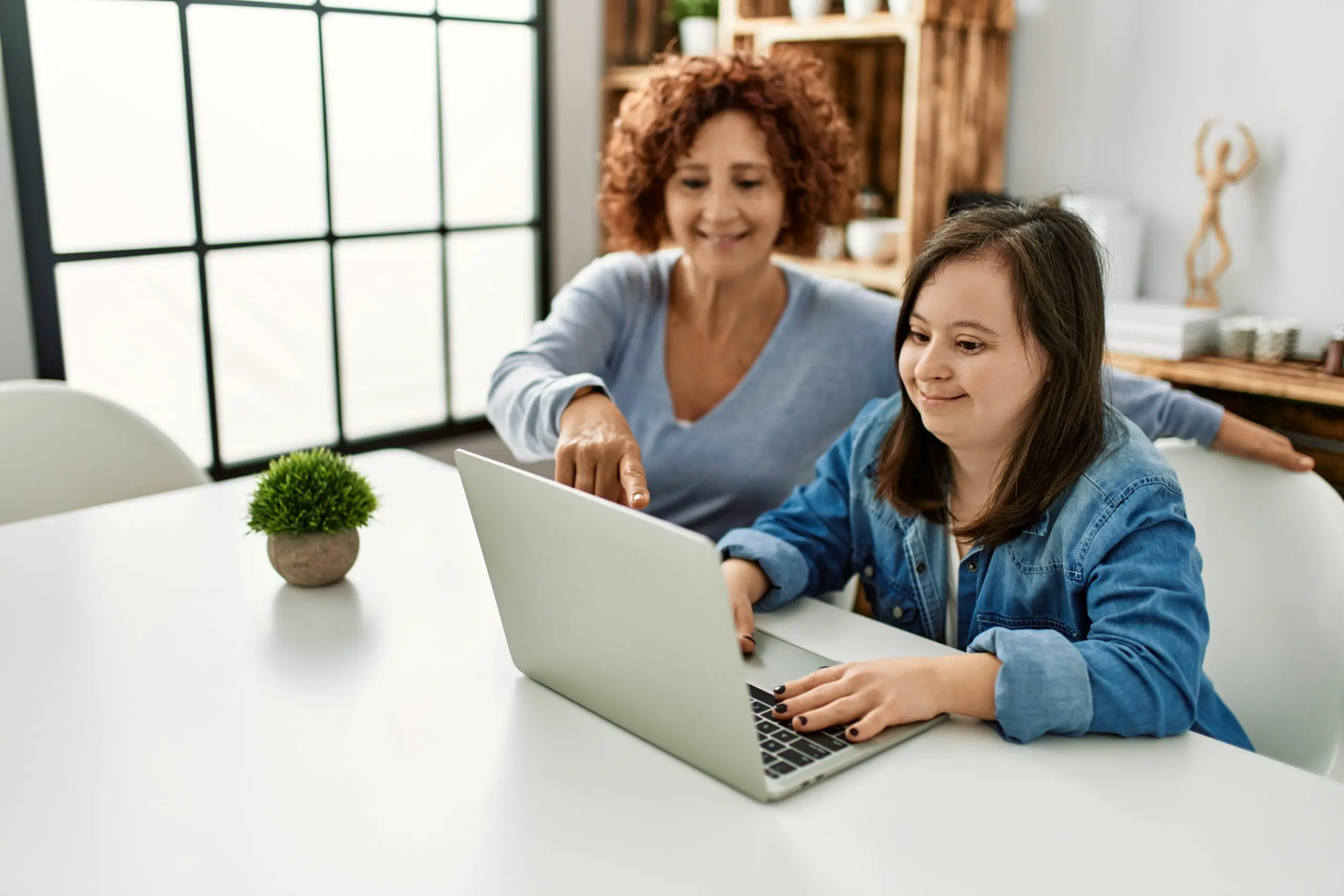 Mature mother and adult daughter with Down syndrome using computer laptop at home